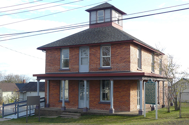 Two-story brick house with a cupola, porch columns, and historical marker in front.