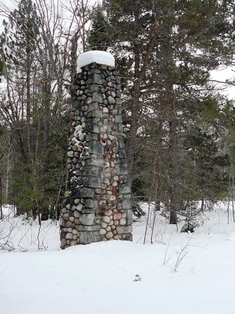 Stone chimney stands in snowy forest, remains of historic CCC camp.