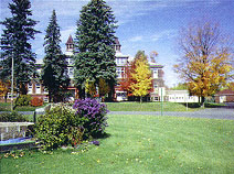 Multi-story building with turrets, autumn trees, and green lawn in the foreground.