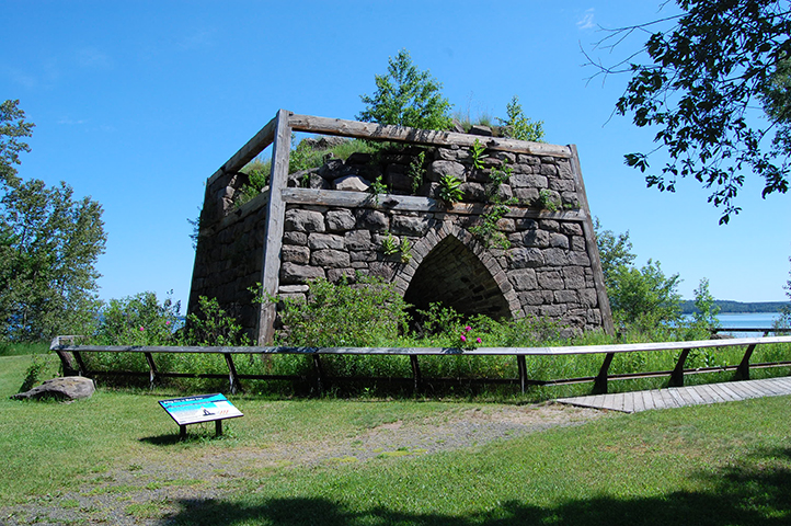 Stone ruins of Bay Furnace surrounded by greenery with a blue sky.