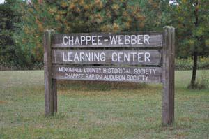 Wooden sign reading “Chappee-Webber Learning Center” stands on grass with trees in the background.