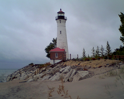 Tall white lighthouse with a red-roofed building on a rocky shoreline under overcast sky.