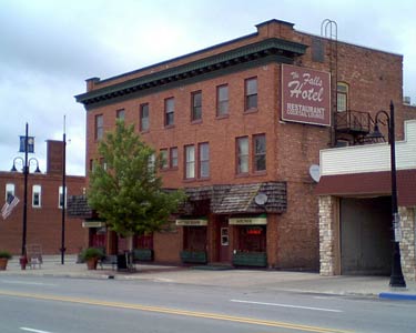 Three-story brick hotel with sign and storefronts on a small-town street.