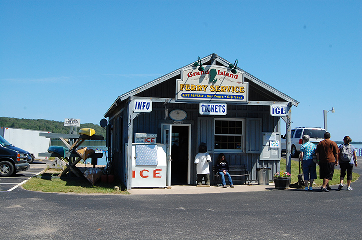 Small wooden ferry ticket building with people walking nearby.