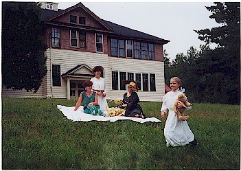 Four children in vintage attire on a lawn, near a historic building.