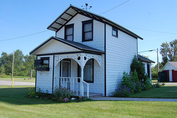 White, tin-sided two-story house with black trim and a small porch on a grassy lot.