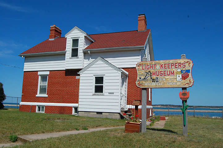 Red brick Light Keeper’s Museum with a wooden sign in front.