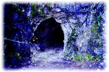 Rough stone mine tunnel entrance in rocky hillside, leading into darkness.