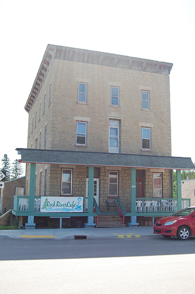 Three-story sandstone hotel with a covered porch and café sign.