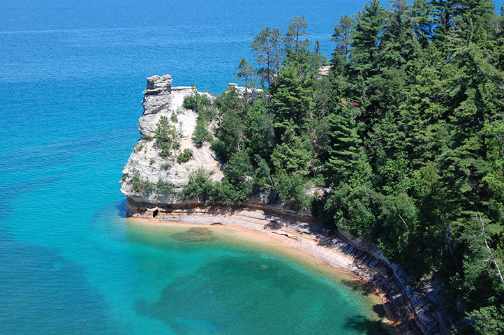 Aerial view of turquoise waters meeting sandstone cliffs at Pictured Rocks.