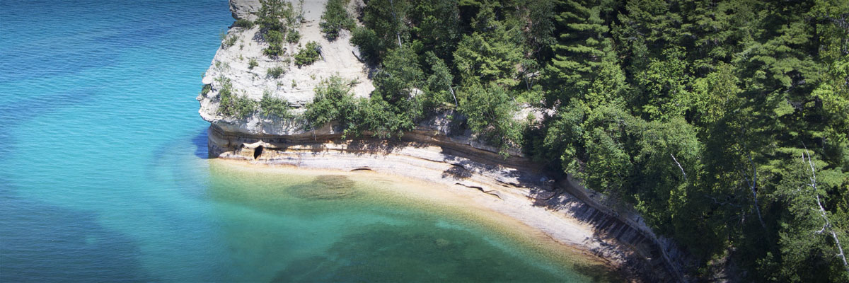 Turquoise waters meet a sandstone cliff surrounded by dense green forest.