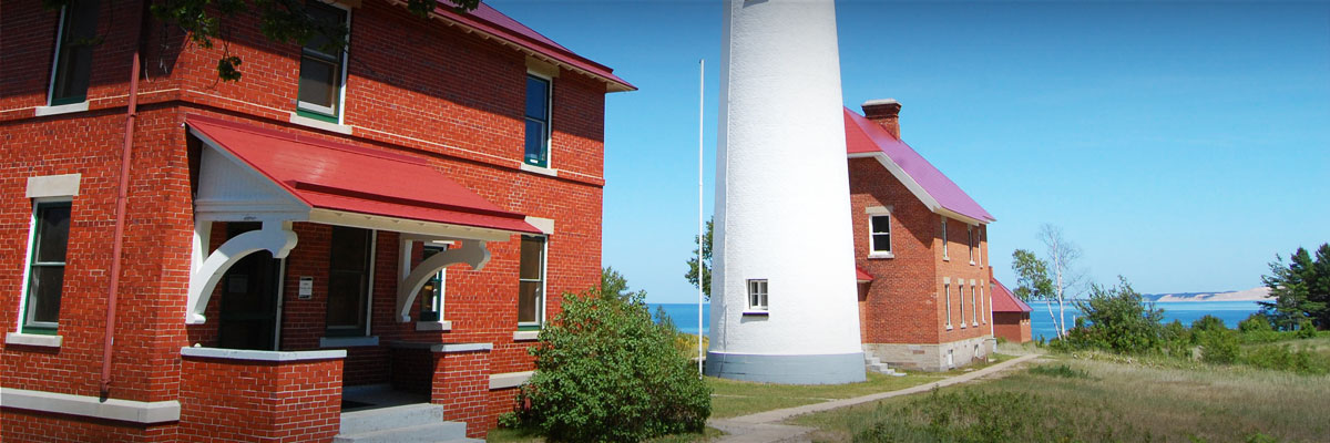 Red brick buildings and a white lighthouse with Lake Superior in the background.