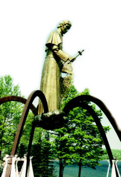 Tall statue of Bishop Baraga with cross and snowshoes overlooking Keweenaw Bay from Red Rocks Bluff.
