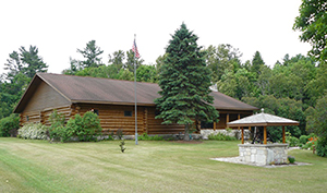 Log museum building with flagpole and stone well at Drummond Island Historical Society site.