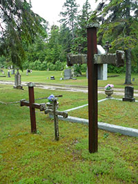 Iron crosses mark graves in a grassy cemetery surrounded by trees near St. Ignace.