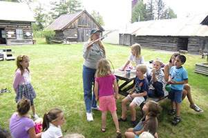 Children gather around a guide at Iron County Museum’s outdoor pioneer and logging exhibit area.