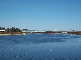 Blue water view of the Manistique Boardwalk and distant bridge under a clear sky.