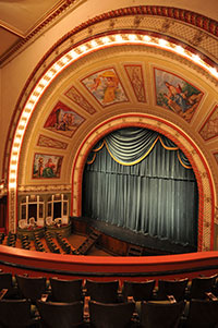  Interior of 1928 Italian Renaissance theater with ornate arch, murals, and velvet stage curtain.