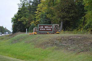 Wooden entrance sign for J.W. Wells State Park surrounded by trees and grass.