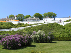 White historic buildings and walls of Fort Mackinac rise above green lawns and blooming lilacs.