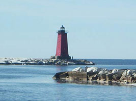 Red lighthouse on a rocky pier extending into the calm blue waters of Lake Michigan.
