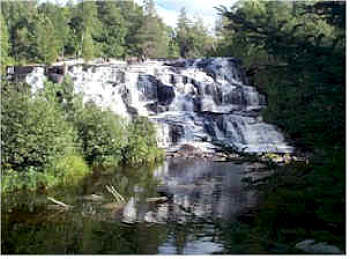 Water cascading over rocky steps at Bond Falls, surrounded by dense green forest.