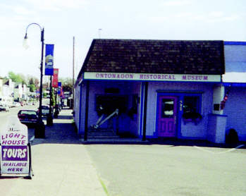 Exterior of the Ontonagon Historical Museum with a lighthouse tour sign on the sidewalk.