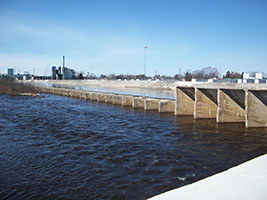 Concrete siphon dam bridge over a dark, fast-moving river under a clear blue sky.